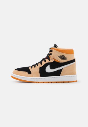Basket montante Air Jordan beige, noire, blanche et orange avec des lacets noirs et le logo ailes Air Jordan sur le côté.