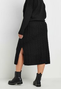 Mustassa neulotussa hameessa on köysimäinen kuvio ja sivuaukeama, yhdistettynä mustiin nauhakenkiin, joissa on hopeiset niitit ja paksu pohja.