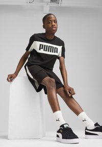 Czarny bawełniany T-shirt z dużym białym logo "PUMA", czarne szorty, białe skarpetki oraz czarne tenisówki z białymi akcentami i logo.