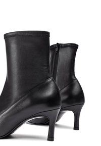 Stivaletti neri in pelle con un design elegante, caratterizzati da un tacco alto e una zip laterale. Texture liscia con dettagli di cucitura discreti.