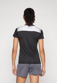 T-shirt de sport noir à manches courtes avec un empiècement en maille blanche. Associé à un short gris, doté d'une taille élastique et d'une texture lisse.