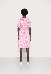 Rosa kortärmad klänning med en texturerad, abstrakt mönster, insvängd midja och nyckelhålsdetalj i ryggen, som faller precis ovanför knäet.