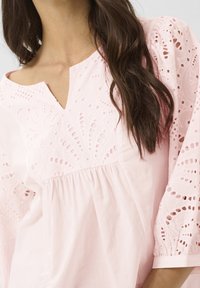 Ljusrosa blus med nyckelhålsutskärning, broderie anglaise-detaljer och puffärmar, med en samlad midja för en löst sittande passform.