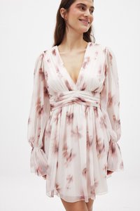 Mini obleka z cvetličnim vzorcem v svetlo roza in kremni barvi. Ima globok V-izrez, dolge napihnjene rokave in nabran pas za strukturo.