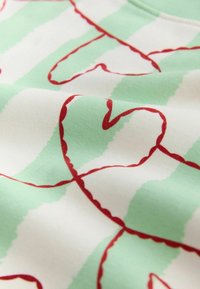 Tissu à larges rayures vert clair et blanc avec des cœurs bordés de rouge reliés par un motif de lignes continues.