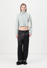 Pull court gris clair avec un col montant, associé à un pantalon large noir avec des coutures blanches contrastantes et un détail de zip.