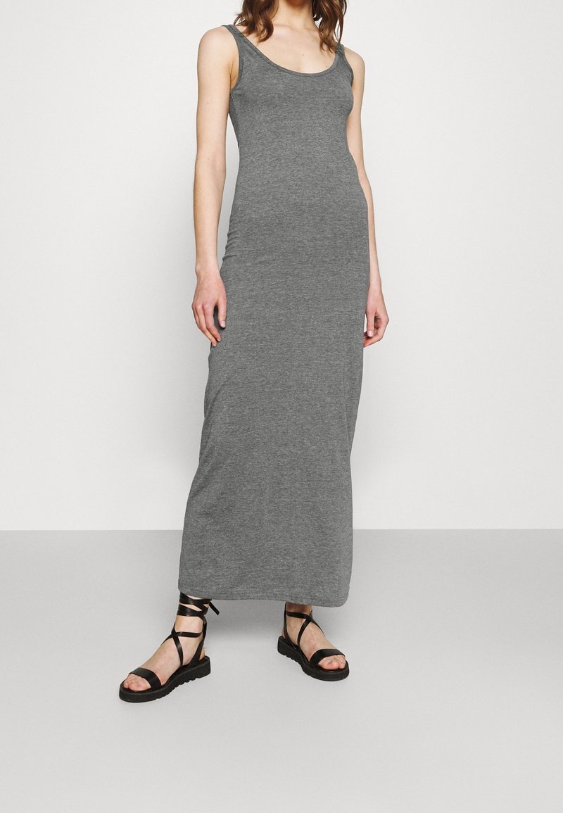 Gray, sleeveless maxi dress made of soft fabric, featuring a round neckline. Paired with black strappy sandals with flat soles.