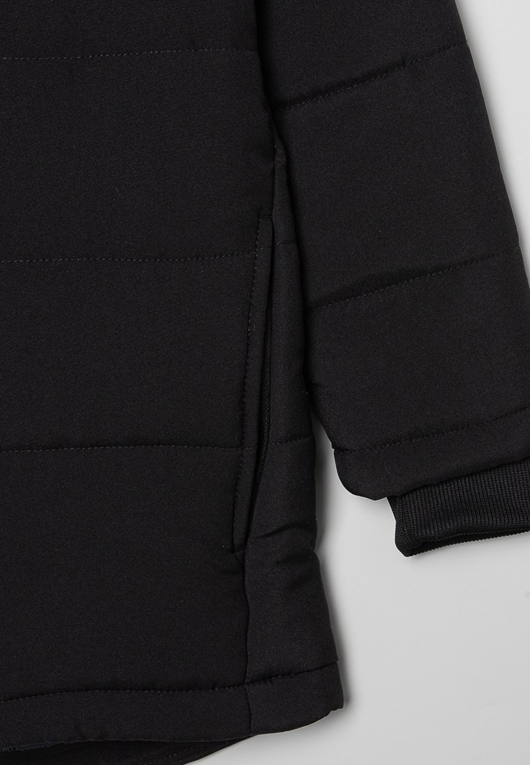 Section de doudoune noire matelassée avec des coutures structurées, des poignets côtelés et une poche latérale zippée. Le tissu présente une texture lisse et mate.