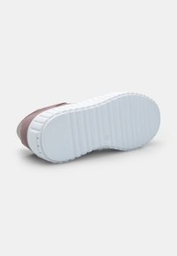 Valge kummist sneakerite talla, millel on horisontaalsed sooned, lilla sametist ülemise osa nähtav külg, pildistatud helesinise tausta ees.