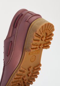 Close-up van een bordeauxleren schoenzool met diepe rubberen noppen en het Timberland-logo in de hiel geperst.