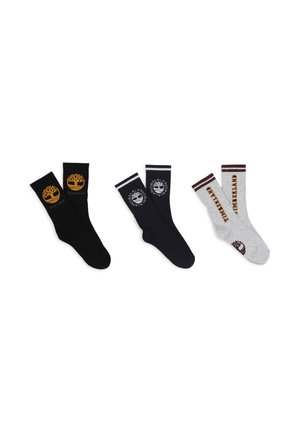Trois paires de chaussettes : noires avec un logo jaune, bleu marine avec un logo blanc et grises avec des accents marron. Toutes présentent des designs de revers et des marques.