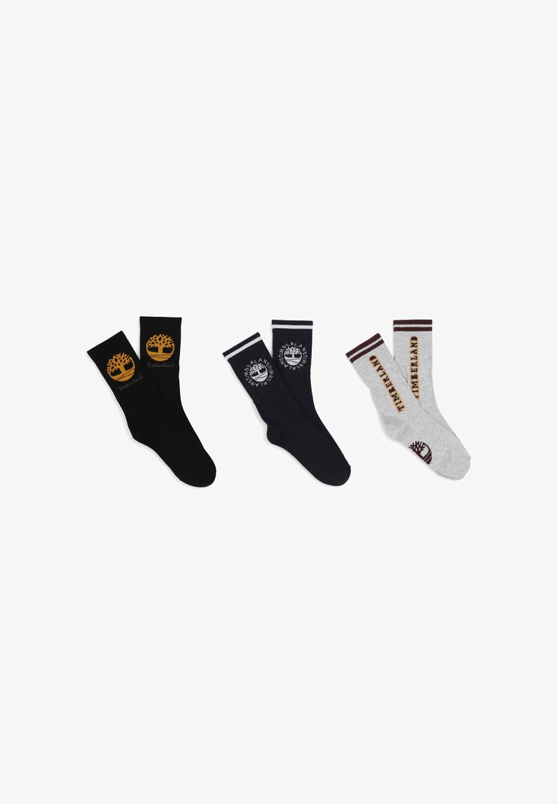 Trois paires de chaussettes : noires avec un logo jaune, bleu marine avec un logo blanc et grises avec des accents marron. Toutes présentent des designs de revers et des marques.