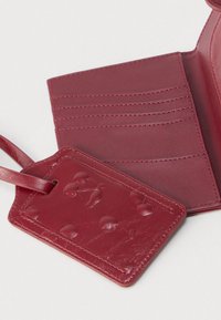 Κόκκινο δερμάτινο πορτοφόλι με πολλαπλές θήκες για κάρτες, λεία υφή και ετικέτα αποσκευών που ταιριάζει, με ανάγλυφο σχέδιο.