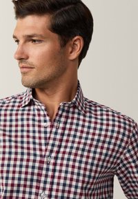 Camicia a quadri bianca, bordeaux e blu navy. Presenta un colletto, chiusura a bottoni e un piccolo dettaglio del logo. Il tessuto appare liscio e leggero.