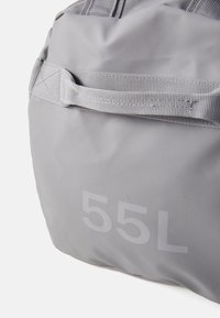 Sac gris avec une finition douce et texturée, arborant un "55L" en blanc bien visible. Comprend une bandoulière durable pour le transport.
