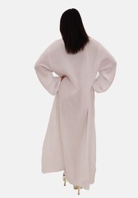 Robe blanche longue et ample en tissu texturé, avec des manches larges et une coupe décontractée, dotée d'une fente dans le dos pour faciliter les mouvements.