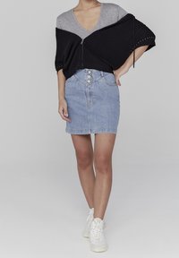 Mustakotoinen vetoketjuhuppari, jossa on puolihihat, harmaa V-kaula-aukko yläosa alla, ja vaaleansininen farkku kynähame, jossa on nappikiinnitys edessä. Yhdistetty valkoisiin lenkkareihin.