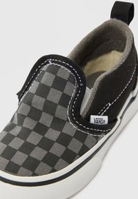 Slip-on sko med sort og gråt ternet mønster i lærredsmateriale, hvid gummisål, kontrastsyning og et mærkelabel på siden.