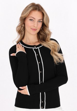 Zwarte cardigan met witte rand, met een knoopsluiting aan de voorkant en lange mouwen. Het materiaal lijkt zacht met ribgebreide manchetten en onderzoom.
