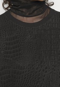 Černá mikina se strukturou krokodýla, s ribbovaným kulatým výstřihem a jemným logem "adidas" v odpovídající černé nitě.