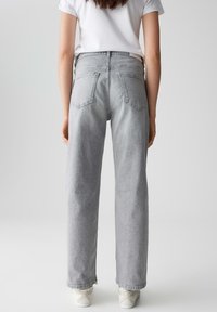 Jeans in denim grigio chiaro con design a gamba dritta, caratterizzati da tasche posteriori e dettagli cuciti, indossati con sneakers bianche.