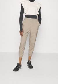 Beige gekürzte Hosen mit elastischen Bündchen, kombiniert mit einem schwarzen Langarmshirt und einem cremefarbenen ärmellosen Top. Schwarze Turnschuhe runden den Look ab.