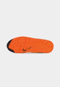 Semelle extérieure d'une basket avec une bande de roulement en caoutchouc orange texturé, une partie noire au talon et un petit logo Nike près de la voûte plantaire.