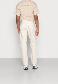 Camiseta de color beige claro con estampado en la parte posterior, combinada con pantalones blancos de pierna recta. Unos zapatos en blanco y negro con detalle de estrella completan el conjunto.