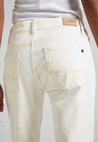 Krämfärgade denimjeans med hög midja, med två bakfickor och en logotyppatch. Tyget har en slät yta med subtila sömnadsdetaljer.