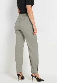 Lichtgrijze broek met een relaxed fit, een elastische tailleband en zijsplitten aan de zoom, gecombineerd met zwarte hoge hakken.