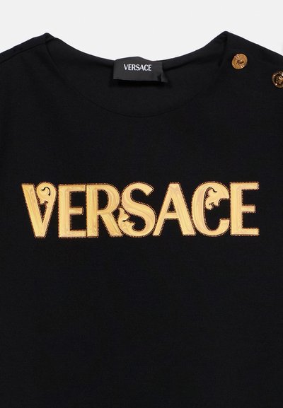 Μαύρο ύφασμα με χρυσό διακοσμητικό κείμενο "VERSACE" στο κέντρο, με διακοσμητικά κουμπιά στην άνω δεξιά περιοχή του ώμου.