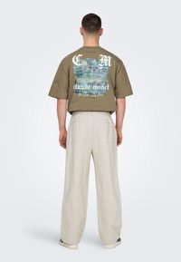 Oliwkowa zielona koszulka z kolorowym nadrukiem Claude'a Moneta na plecach. Do kompletu luźne beżowe spodnie z bocznymi kieszeniami.