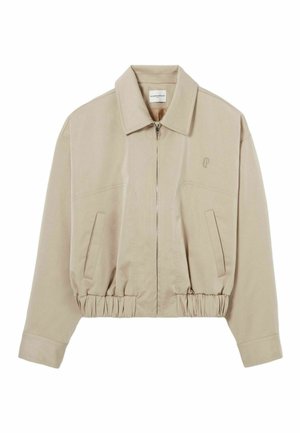 Giacca beige cropped con colletto a risvolto, chiusura con zip, orlo elasticizzato e due tasche frontali. Presenta un logo ricamato discreto sul petto.