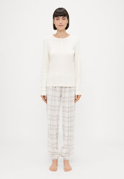 Lange mouw crèmekleurige top met knoopdetail en lichtgrijze geruite pyjamabroek, met een elastische tailleband en manchetten.