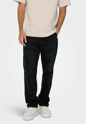 Black denim jeans with straight cut, featuring stitching details. Paired with a beige t-shirt and white sneakers.