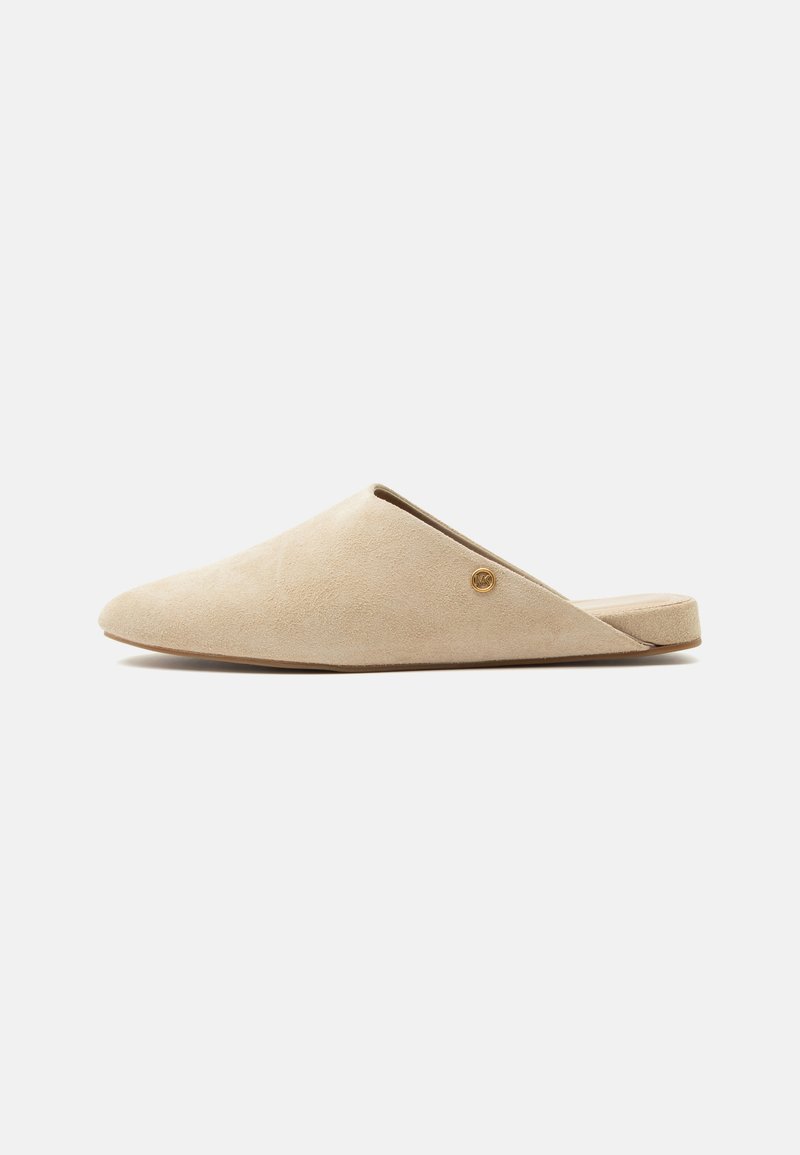 Μπεζ mule επίπεδη slip-on με μυτερή μύτη και μικρή στρογγυλή χρυσή λεπτομέρεια λογότυπου στη πλευρά, σε απλό λευκό φόντο.
