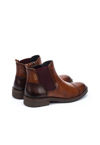 Botas de tobillo de cuero marrón con paneles elásticos en los laterales, puntera redondeada, tacón oscuro en contraste y suela de goma texturizada. Sin marcas visibles.