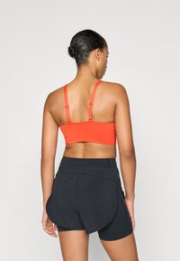 Sujetador deportivo rojo con tirantes delgados ajustables, combinado con pantalones cortos negros que presentan un diseño en capas y una cintura elástica.
