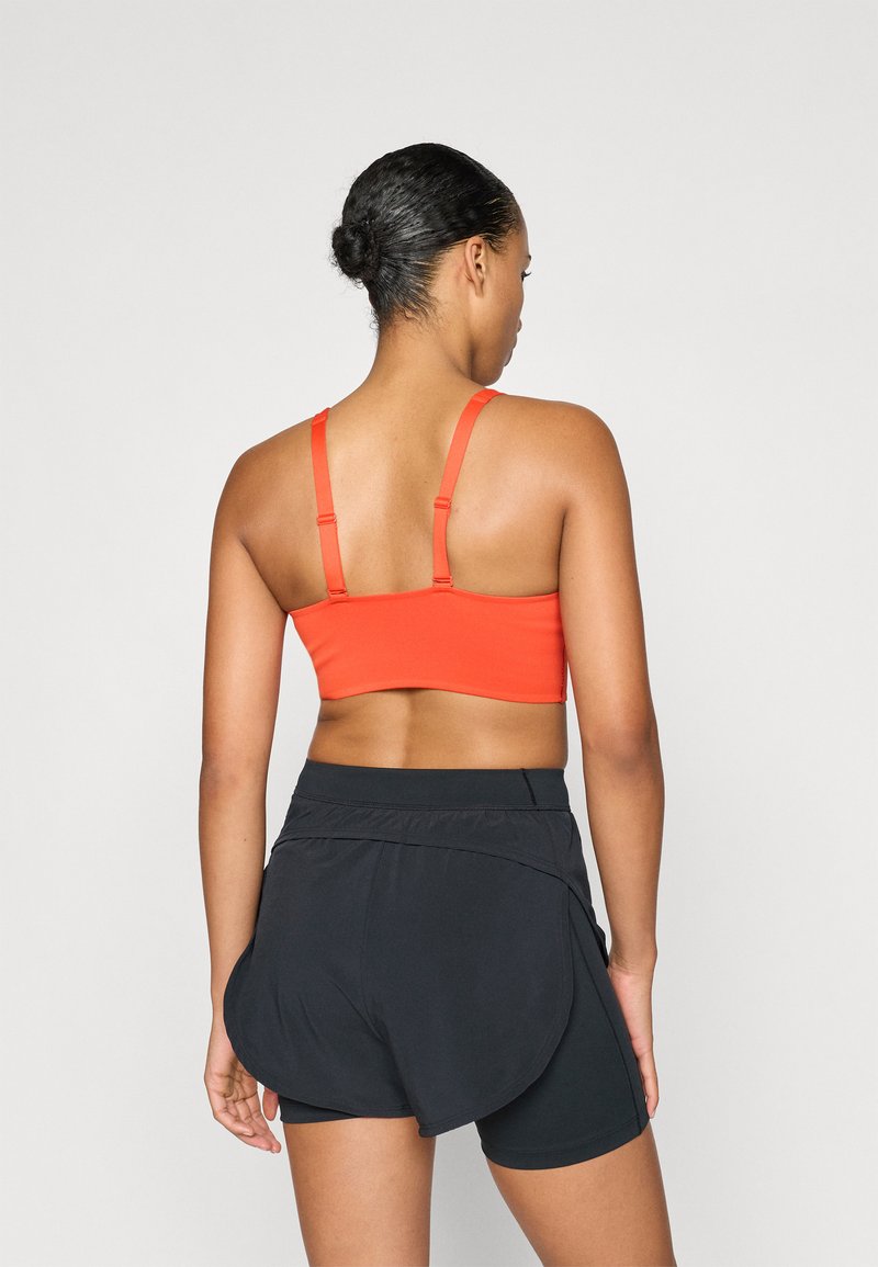 Rode sportbeha met dunne verstelbare bandjes, gecombineerd met zwarte shorts met een gelaagd ontwerp en een elastische tailleband.