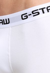 Boxer briefs bianchi con un logo G-STAR nero su una vita elasticizzata bianca, tessuto liscio e dettagli di cucitura visibili.