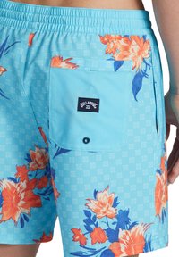 Shorts de înot de culoare albastru deschis, cu un model floral în nuanțe de portocalie și albastră, având un buzunar pe spate cu un nasture și eticheta mărcii.