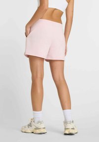 Pantalones cortos de sudadera rosa claro con cintura elástica, bolsillos laterales y un corte relajado, combinados con calcetines blancos hasta el tobillo y zapatillas deportivas beige.