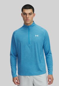 Lichtblauwe lange mouwen zip-up top van textuurstof, met eenstaande kraag en een wit logo op de borst.