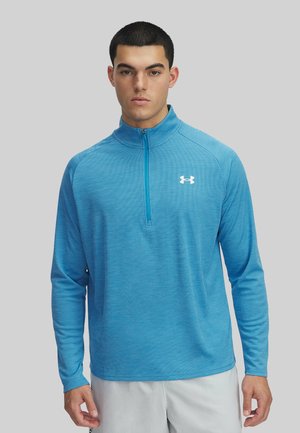 Lichtblauwe lange mouwen zip-up top van textuurstof, met eenstaande kraag en een wit logo op de borst.