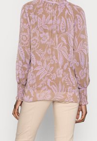 Blusa leggera a fantasia floreale beige con motivi lavanda, maniche lunghe con polsini arricciati e un collo raccolto delicato.