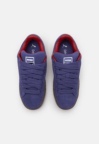 Paarse suède sneakers met bruine rubberen zolen, met rode accenten aan de binnenkant en een traditionele vetersluiting. PUMA-logo zichtbaar.