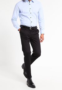 Ljusblå långärmad skjorta med svarta knappar, tillsammans med svarta kostymbyxor och svarta läderstövlar, med en skräddarsydd passform.