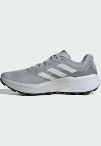 Zapatilla deportiva de un gris claro con parte superior de malla, franjas acentuadas blancas, suela acolchada y suela negra resistente para tracción.
