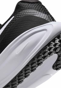 Gros plan du talon d’une chaussure de sport noire et blanche montrant une semelle texturée et une tige en tissu avec un logo discret de la marque sur la semelle intermédiaire blanche.