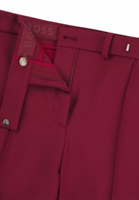 Bordowe spodnie o gładkiej fakturze, z zapięciem na guzik, zamkiem błyskawicznym oraz szlufkami na pasek. Podszewka w pasie z subtelnym nadrukiem logo.